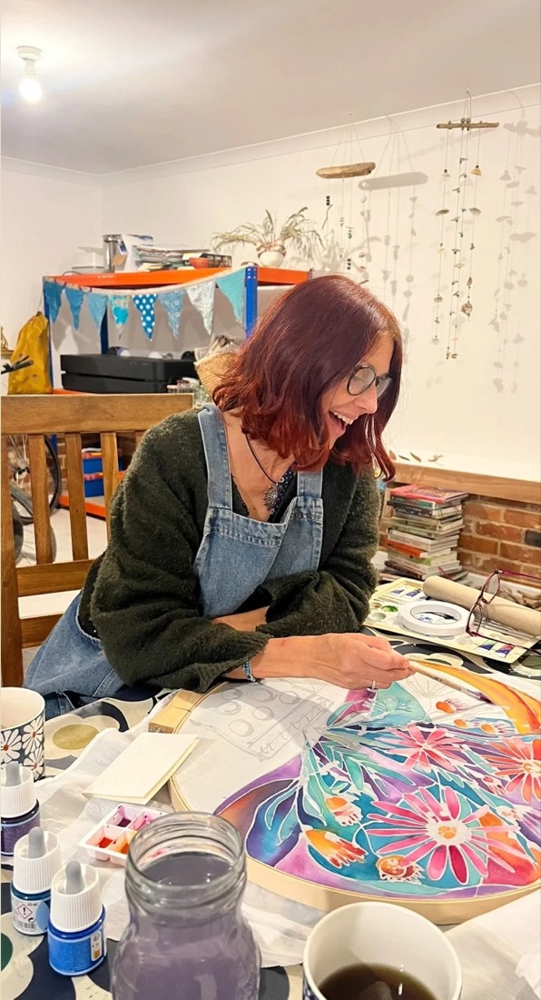 Natalie laughing as she paints a bright silk flower design at her studio table