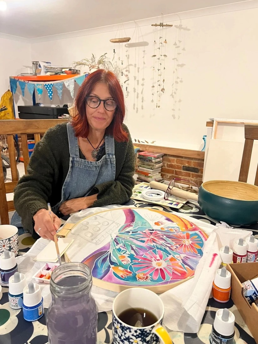 Natalie smiling at her studio table, painting a large silk design