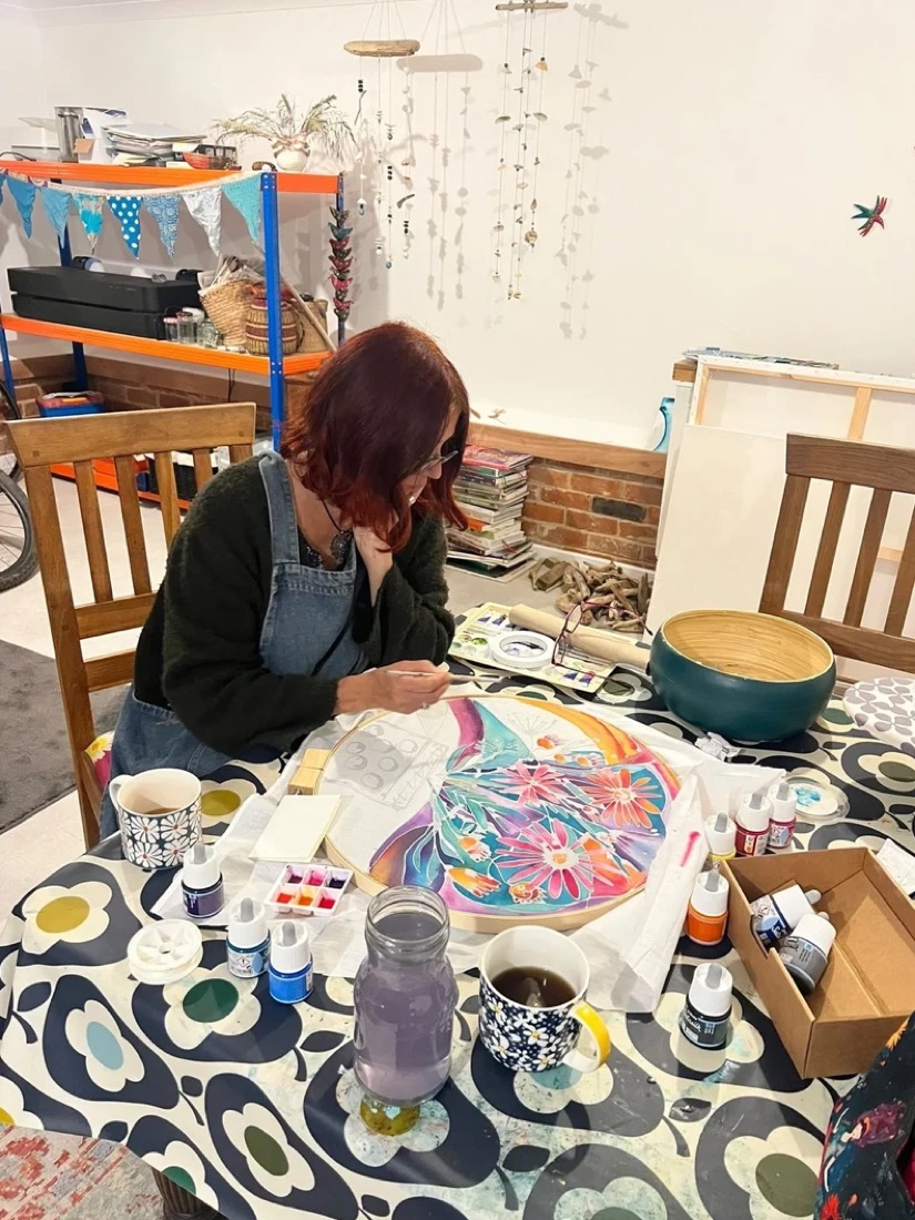 Natalie painting silk at a patterned table in her studio, with paints and a cup of tea beside her
